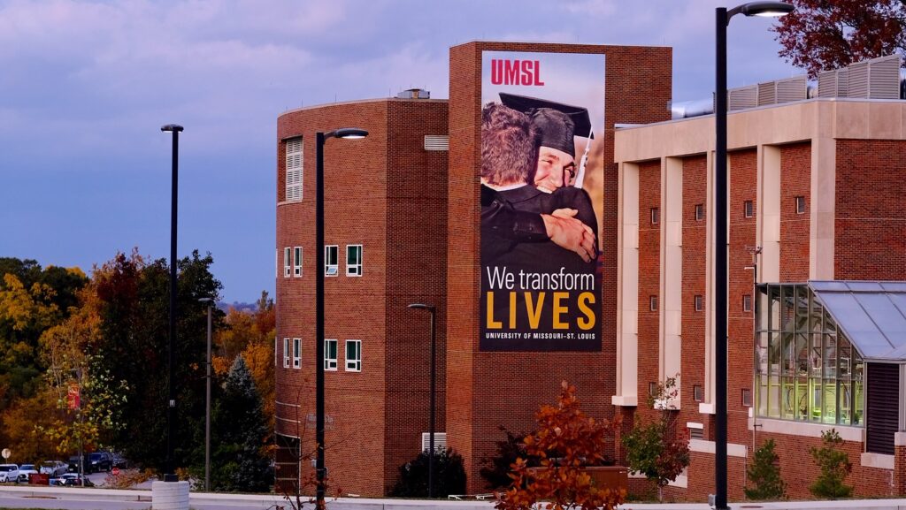 We Transform Live Vertical banner with Graduate Hugging other.